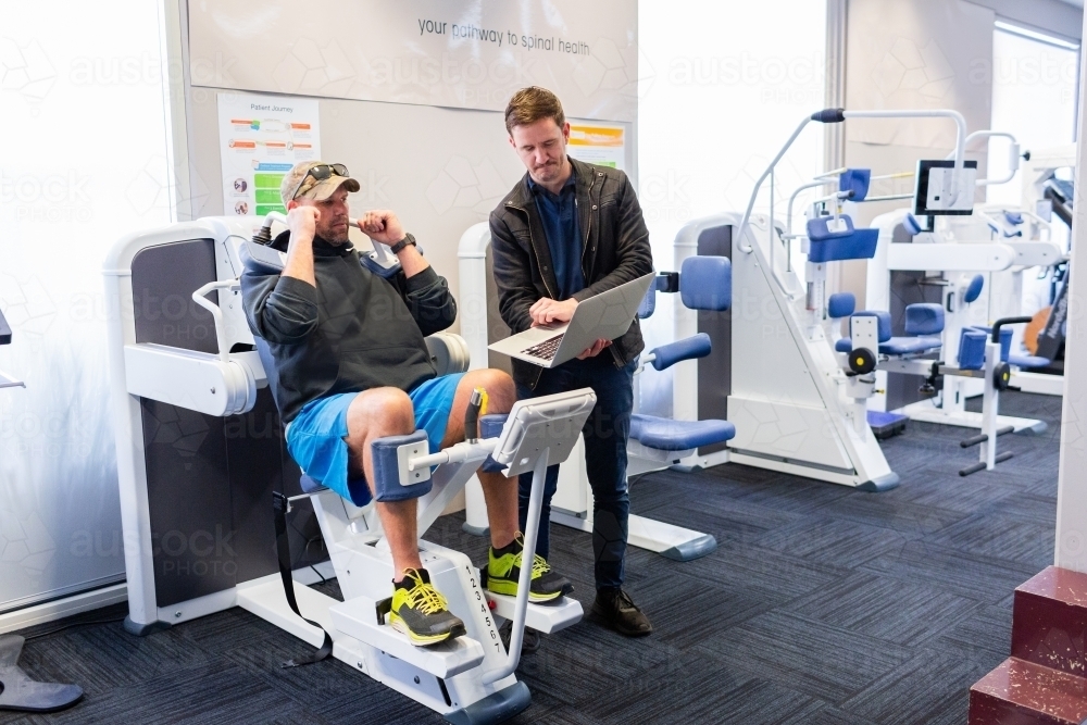 exercise therapy equipment at physiotherapy clinic with men discussing progress - Australian Stock Image