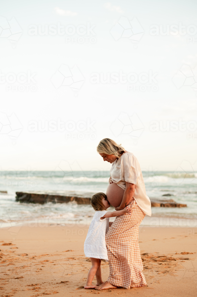Expectant mother embraces child on beach at sunset - Australian Stock Image