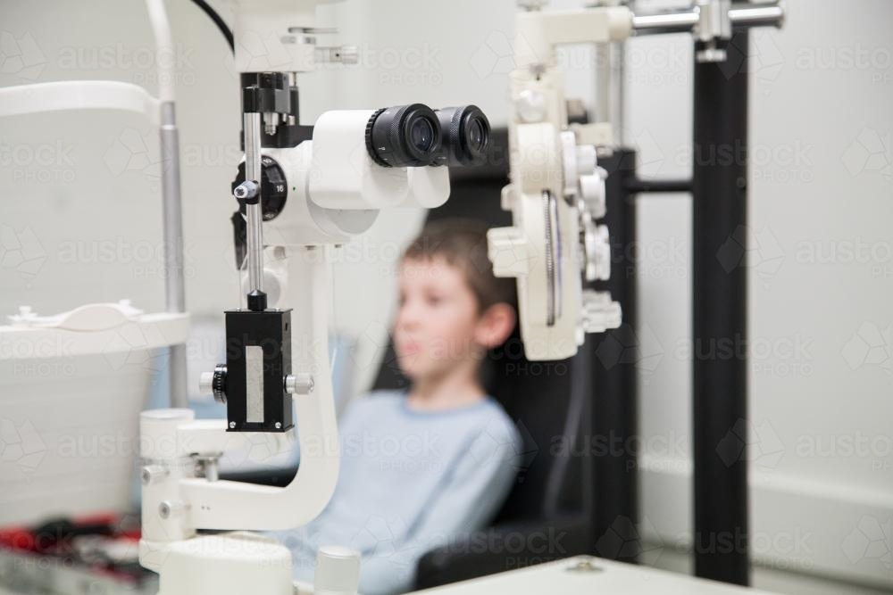 Eye testing machines and boy in chair in an optometrist's white room - Australian Stock Image