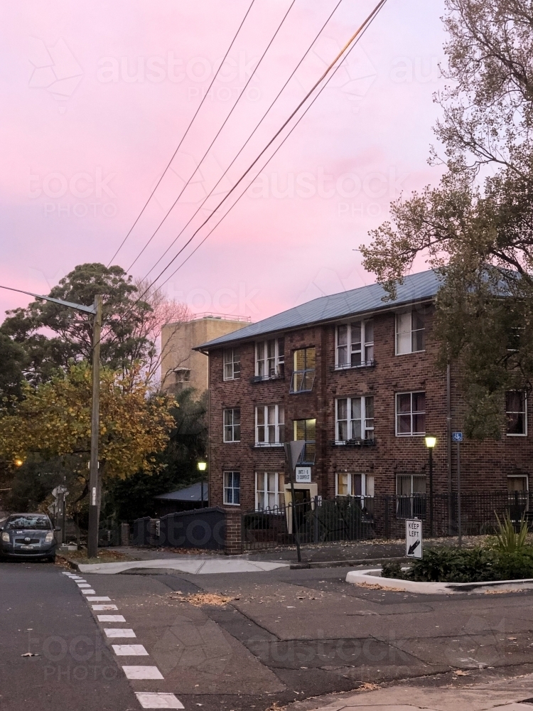 facade of a building made of bricks with power lines and trees on the side with pink skies - Australian Stock Image