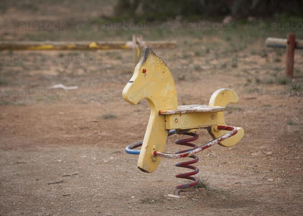 Faded yellow rocking horse at park playground - Australian Stock Image