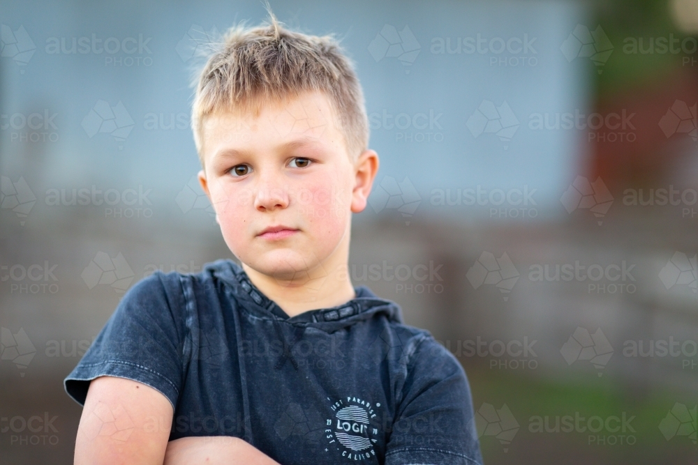 Fair young boy with arms crossed standing outdoors - Australian Stock Image