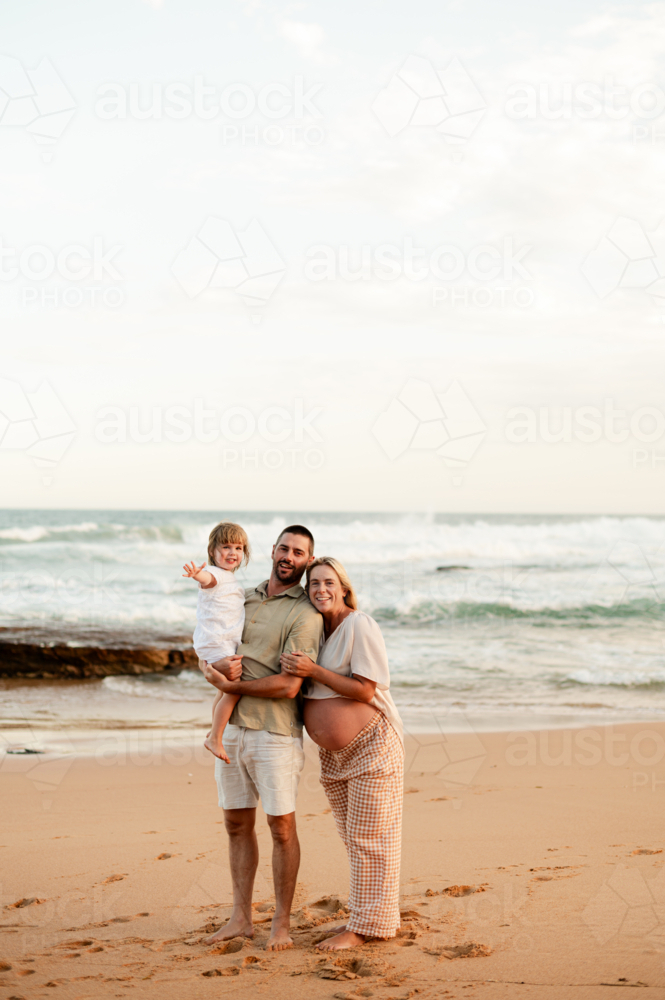 Family enjoying sunset on a beach with expecting mother and playful child - Australian Stock Image