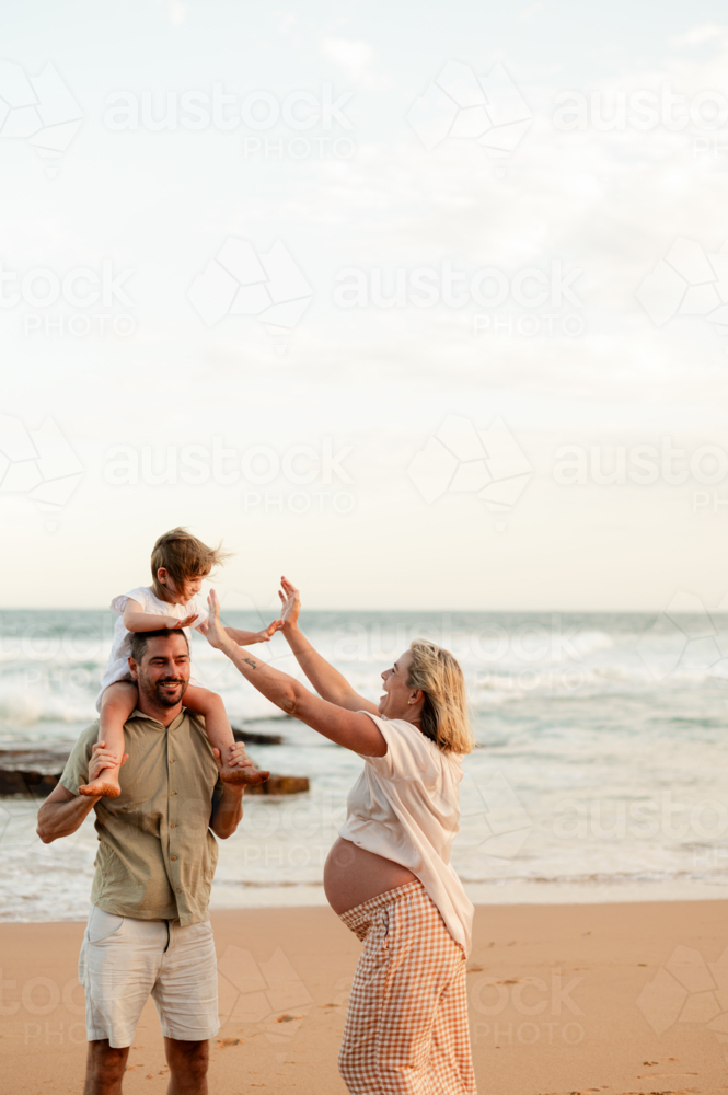 Family enjoying sunset on beach with pregnant woman and child playing outdoors - Australian Stock Image