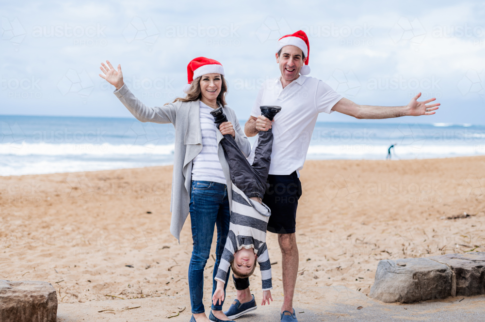 Family joyfully celebrating Christmas on the beach, wearing Santa hats - Australian Stock Image