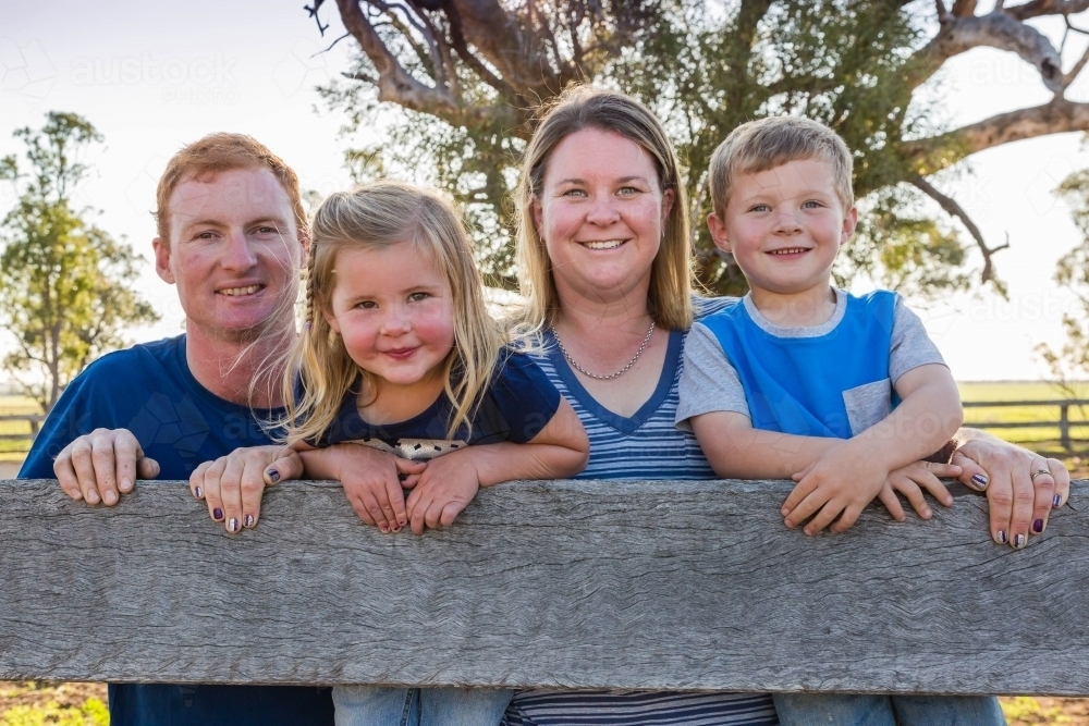 Family leaning on wooden fence on farm - Australian Stock Image