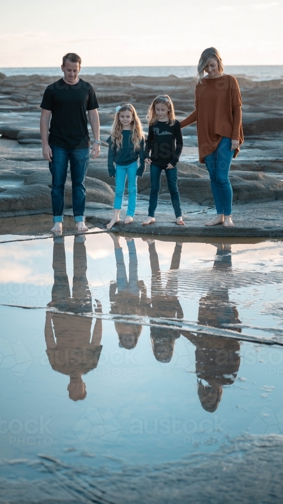 Family of four looking into reflection in beach rockpool - Australian Stock Image