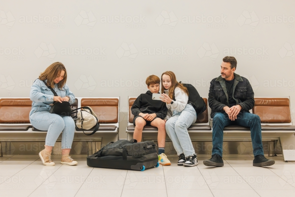 Family of four sitting together in departures lounge at airport waiting for flight - Australian Stock Image