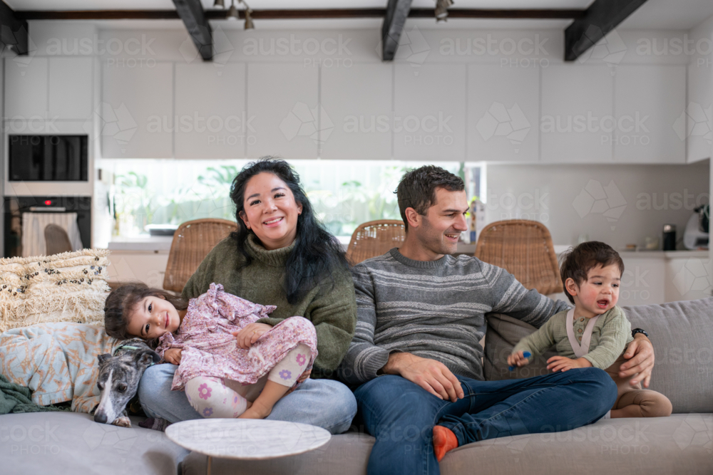 Family of Four Sitting Together on Couch in Living Room : Austockphoto Family of Four Sitting Together on Couch in Living Room - Australian Stock Image