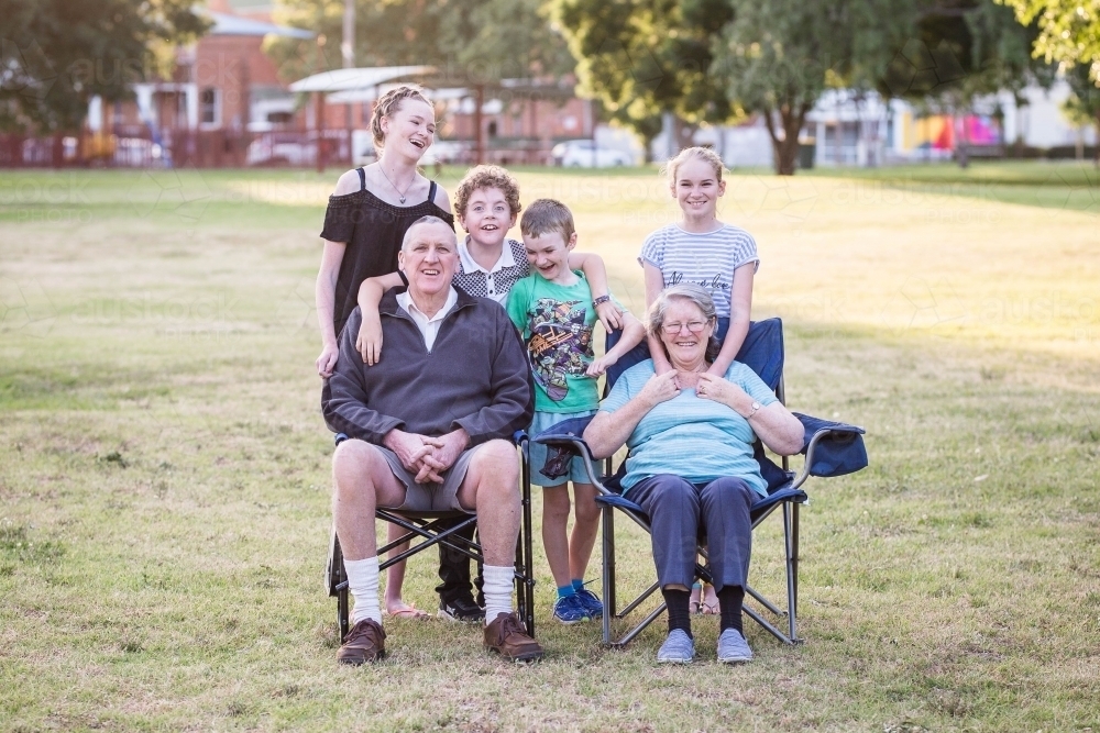 Family of grandparents sitting on chairs with grandchildren laughing - Australian Stock Image