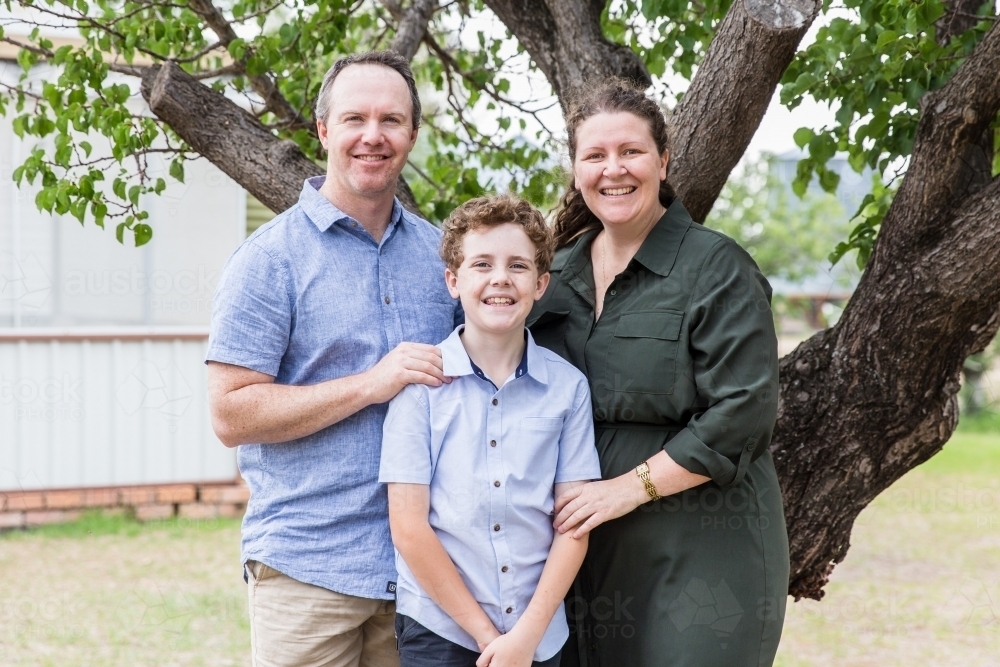 Family of three standing together in back yard at home smiling - Australian Stock Image