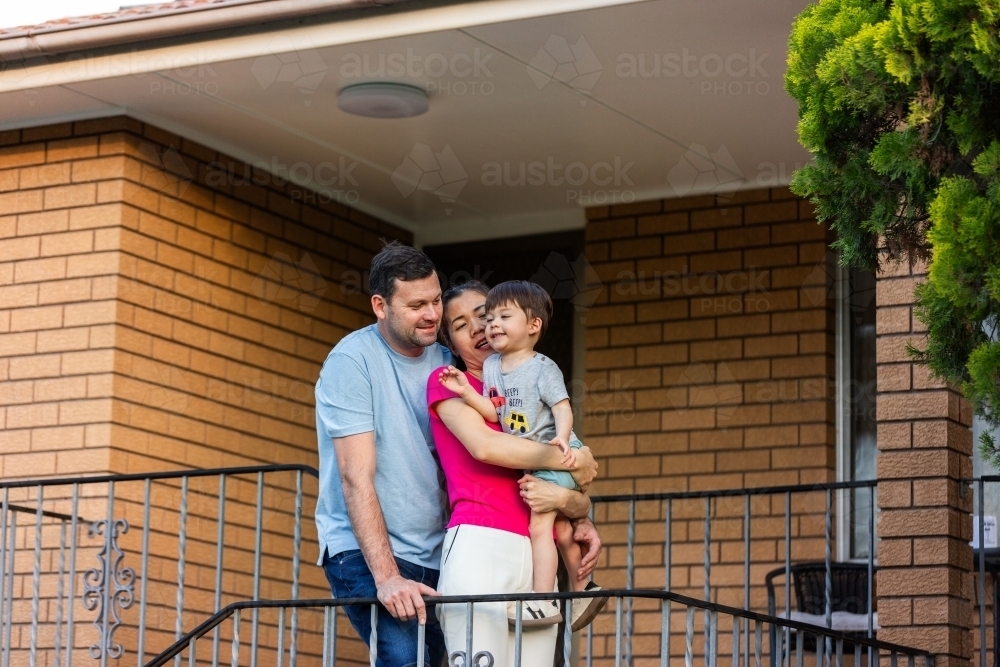 Image of Family of three together on stairs at front of brick home ...