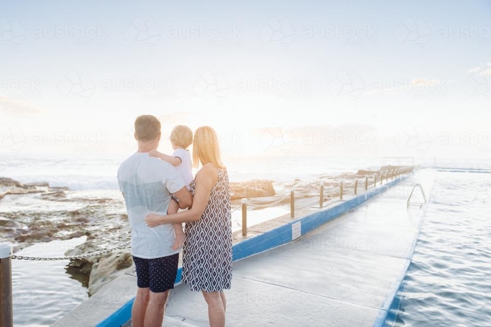 Family of three watching the sunrise at the beach - Australian Stock Image