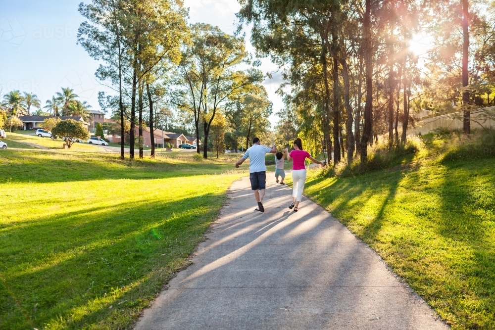 Family of three with toddler on suburban walk in golden afternoon light - Australian Stock Image