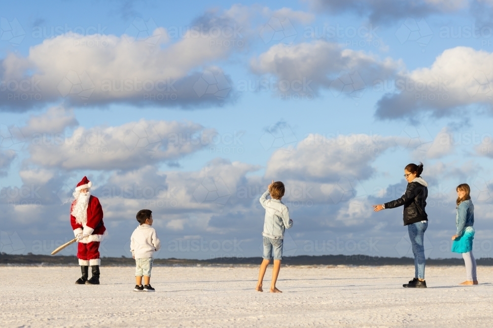 family playing beach cricket with child preparing to bowl to a man dressed as santa - Australian Stock Image