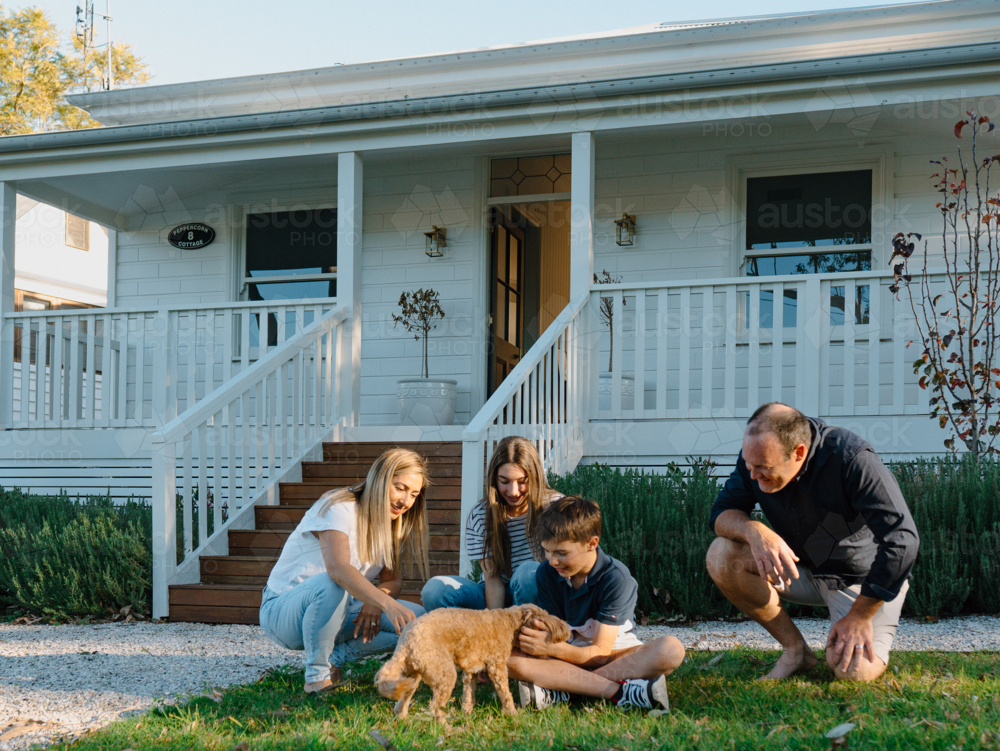 Family playing with their dog in the front yard of the house. - Australian Stock Image