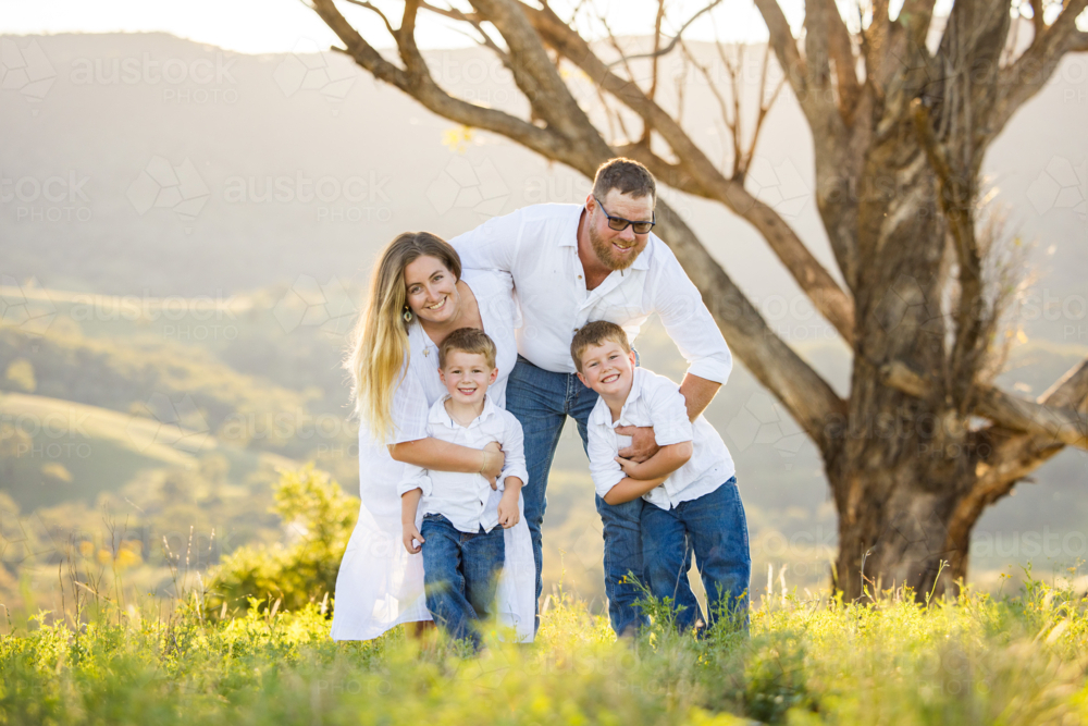 Family portrait on hilltop with lush green landscape at sunset - Australian Stock Image