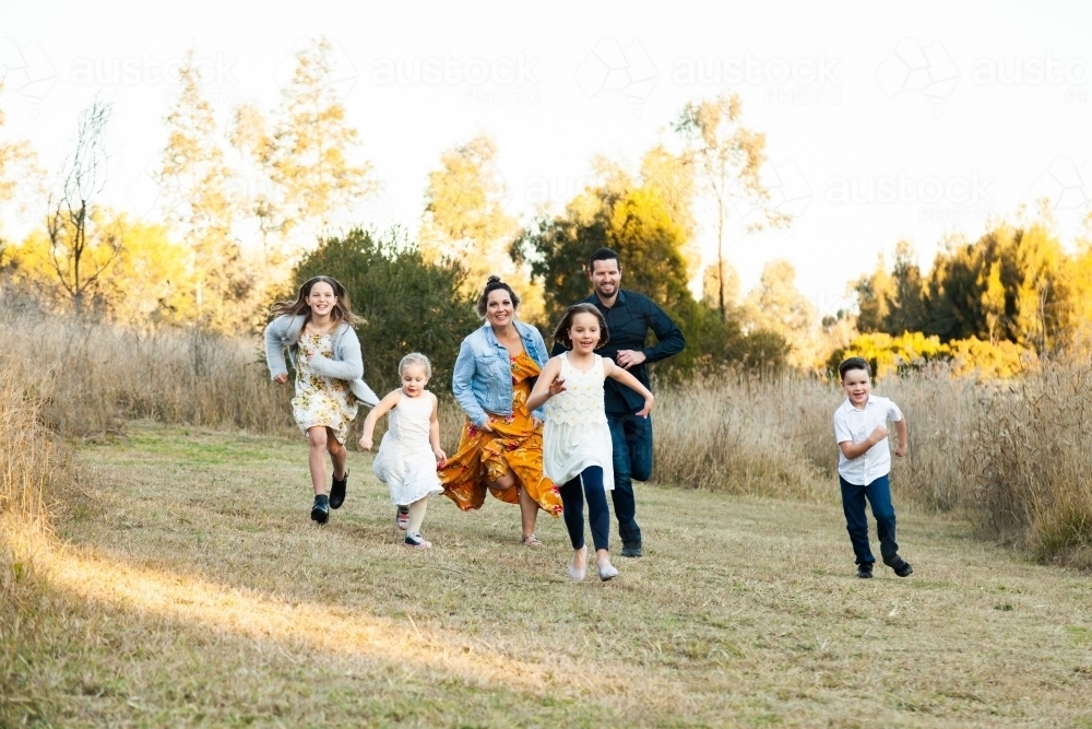 Family running in park, parents chasing children - Australian Stock Image