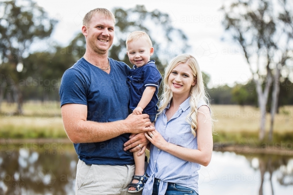 Family standing near water in dam on farm smiling - Australian Stock Image