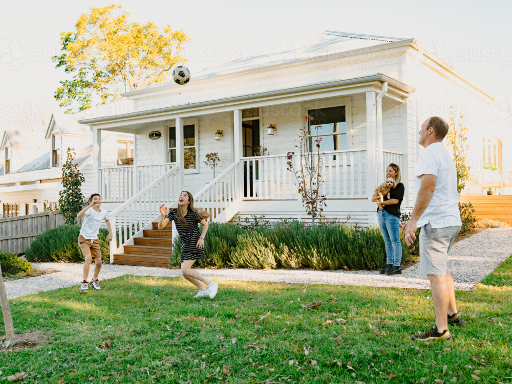 Family tossing a soccer ball inside their yard. - Australian Stock Image
