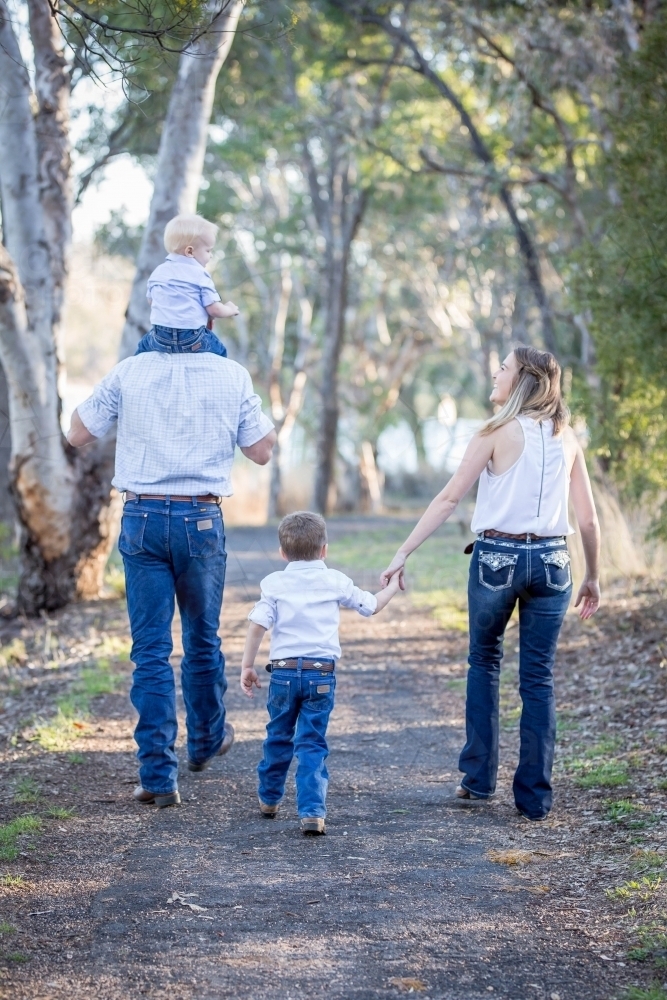 Family walking with baby being carried on father's shoulders while mother holds son's hand - Australian Stock Image