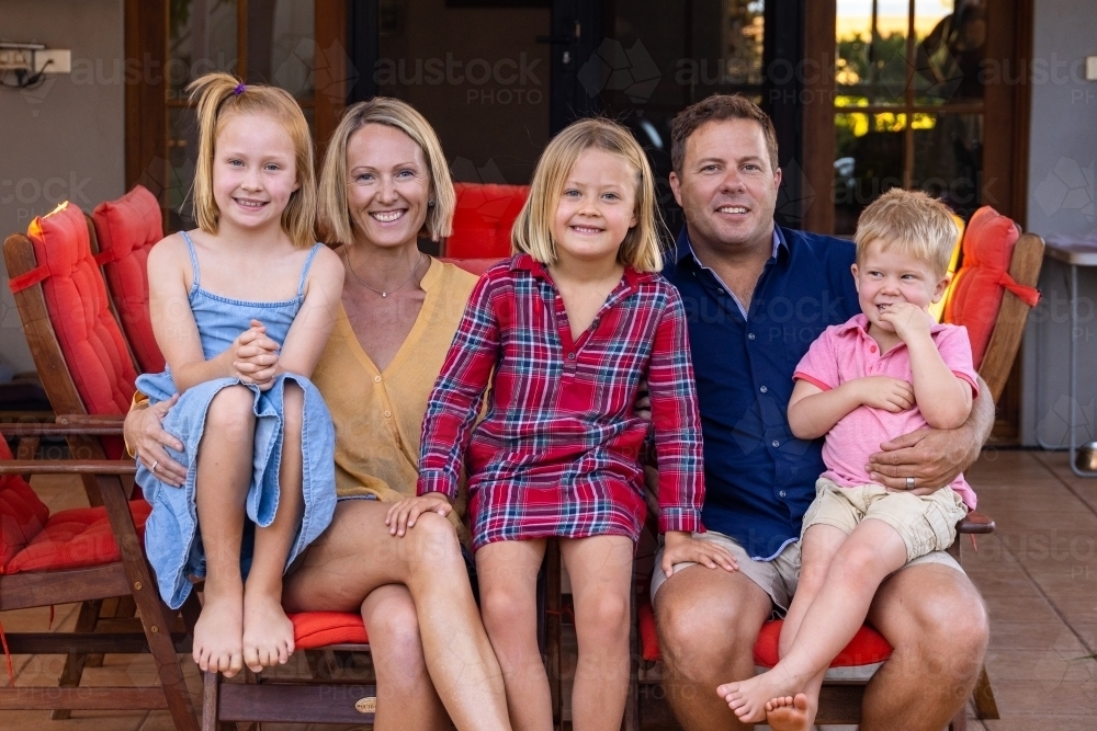 family with three young children sitting outside their home - Australian Stock Image