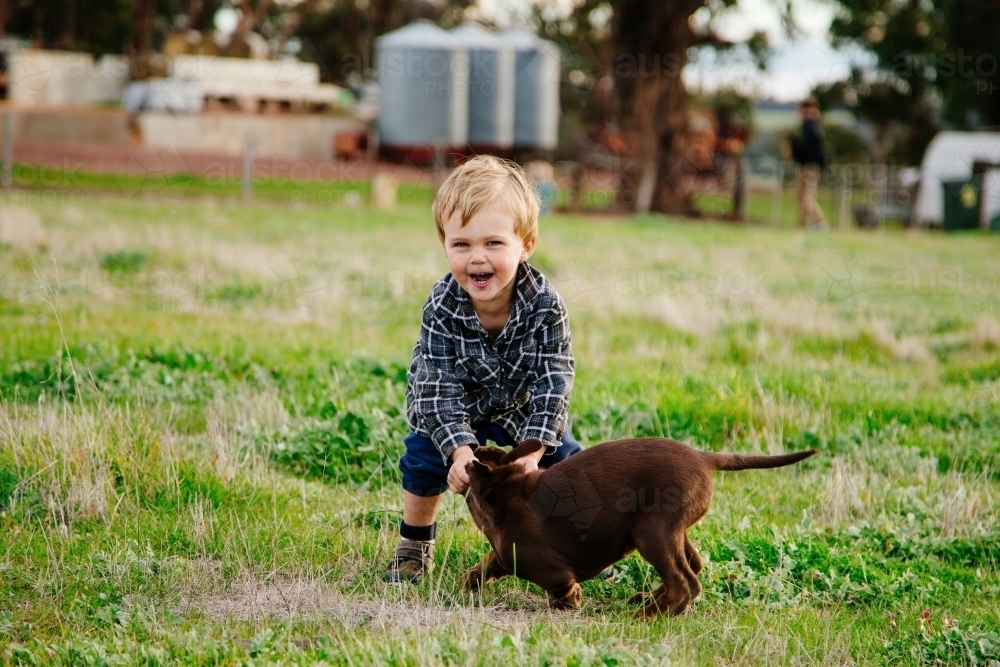 Farm boy plays with kelpie puppy - Australian Stock Image
