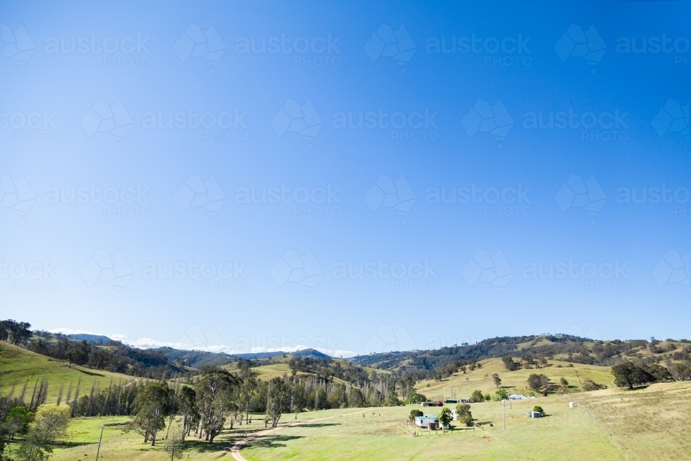 Farm in green valley under clear blue sky - Australian Stock Image