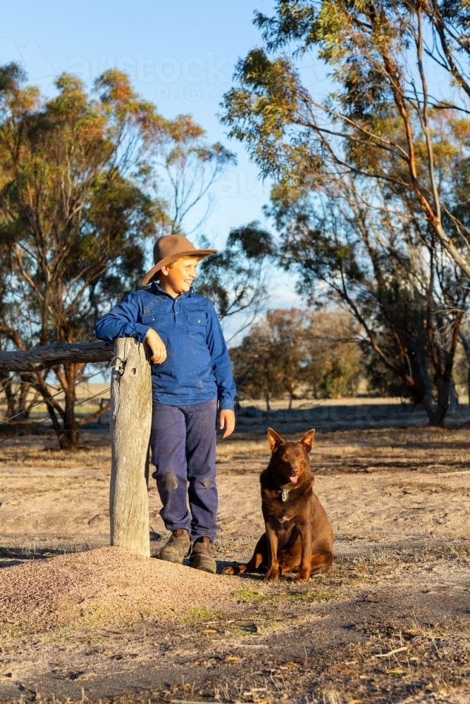 farm kid leaning on post with his red kelpie dog by his side - Australian Stock Image