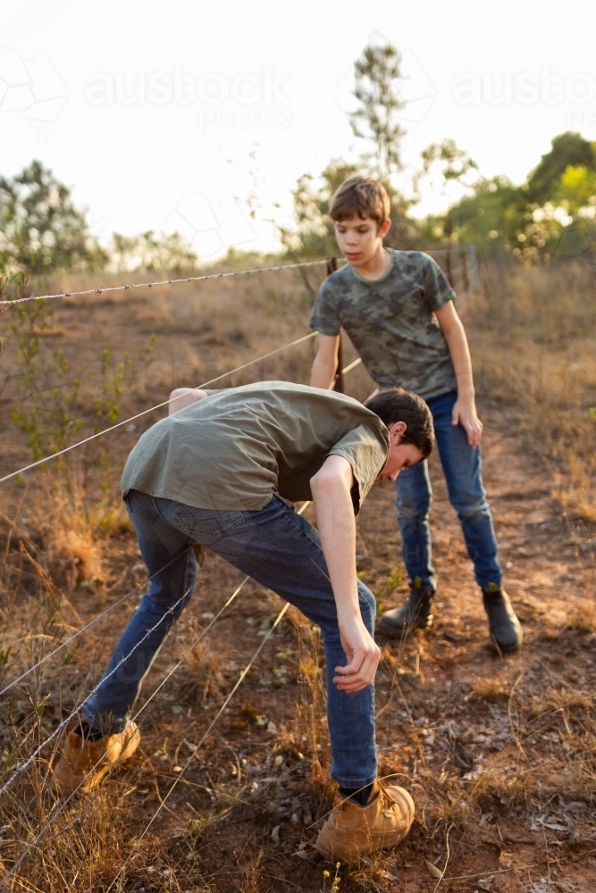 Farm kids climbing through wire fence helping one another - Australian Stock Image