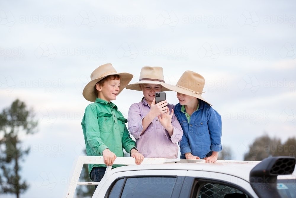 Farm kids taking photos with their phone on the back of a ute - Australian Stock Image