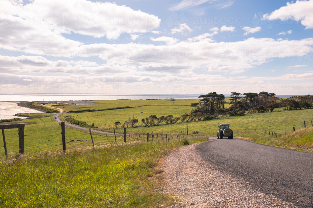 Farm tractor with hay bale driving on the coastal country road. - Australian Stock Image