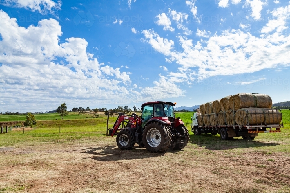 Farm tractor with trailer of hay bales on sunlit Aussie farm - Australian Stock Image