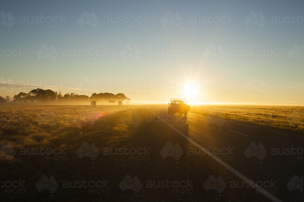 Farm ute driving into sun on country highway - Australian Stock Image