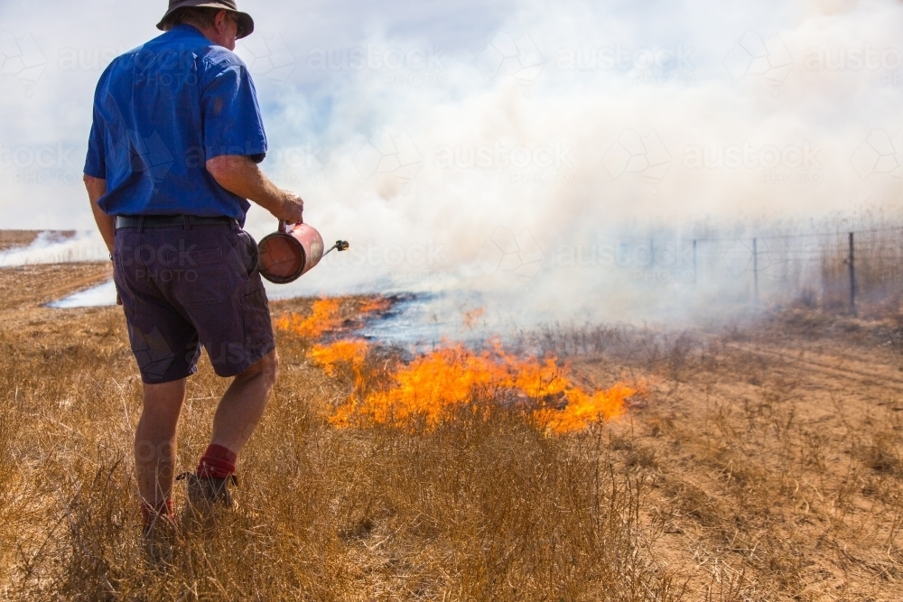 Farmer carrying a fire lighter burning grass - Australian Stock Image
