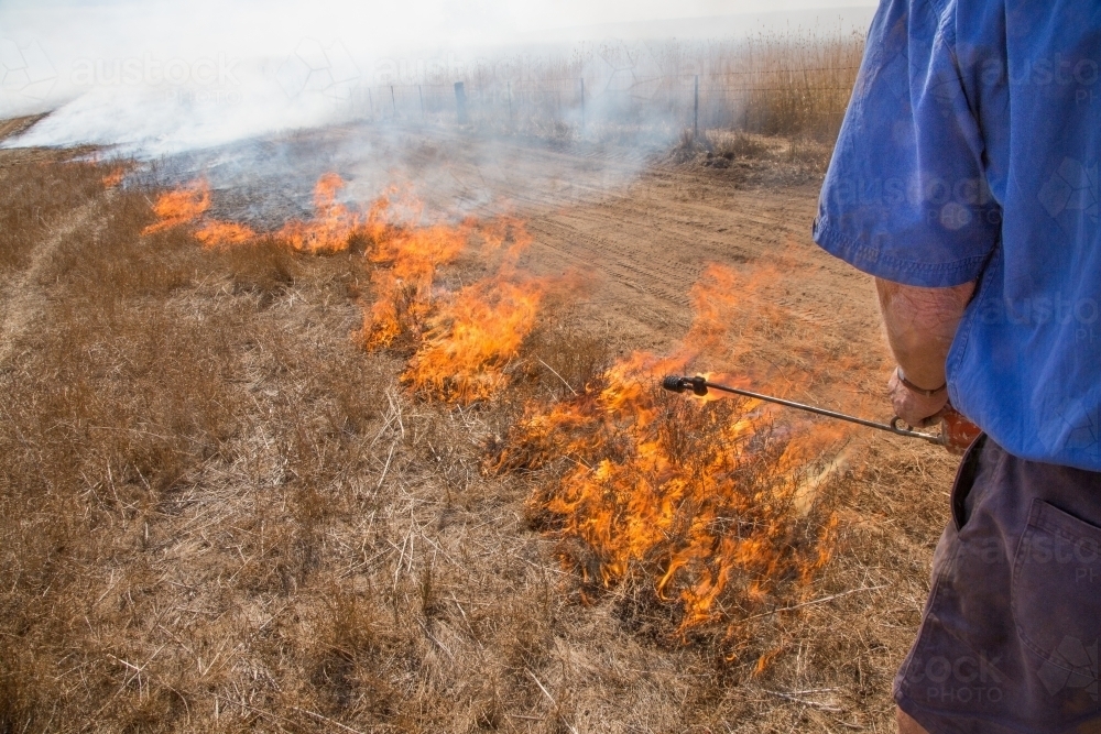 Farmer carrying a fire lighter burning grass - Australian Stock Image