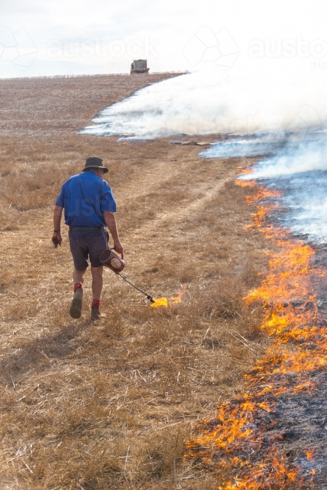 Farmer carrying a fire lighter burning grass - Australian Stock Image