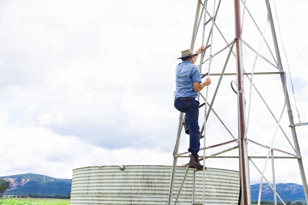 Farmer climbing up farm windmill to check and repair pump - Australian Stock Image