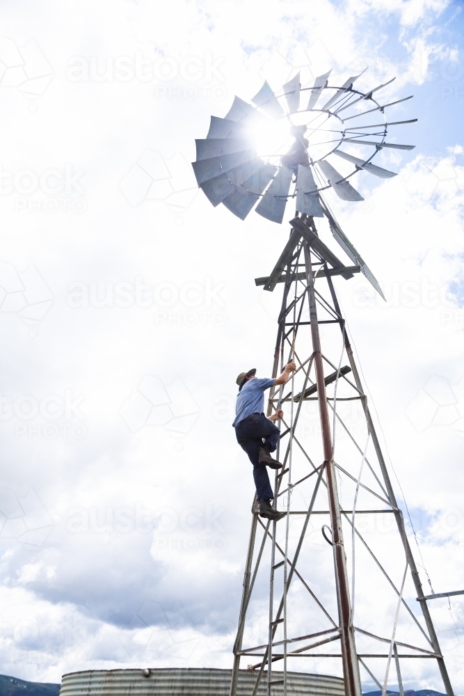 Farmer climbing up farm windmill to check and repair pump - Australian Stock Image