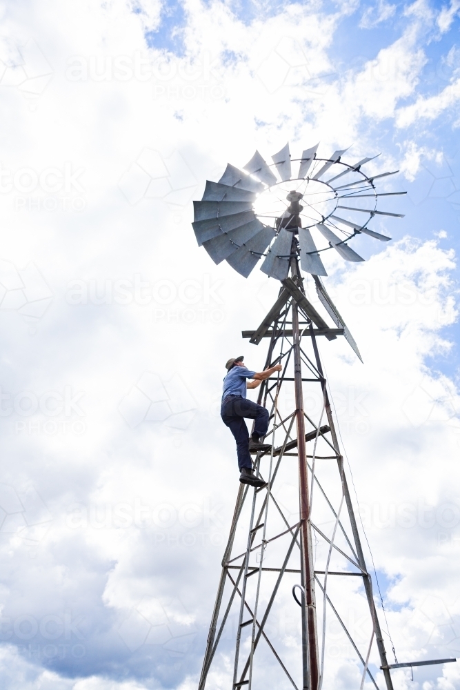 Farmer climbing up farm windmill to check and repair pump - Australian Stock Image