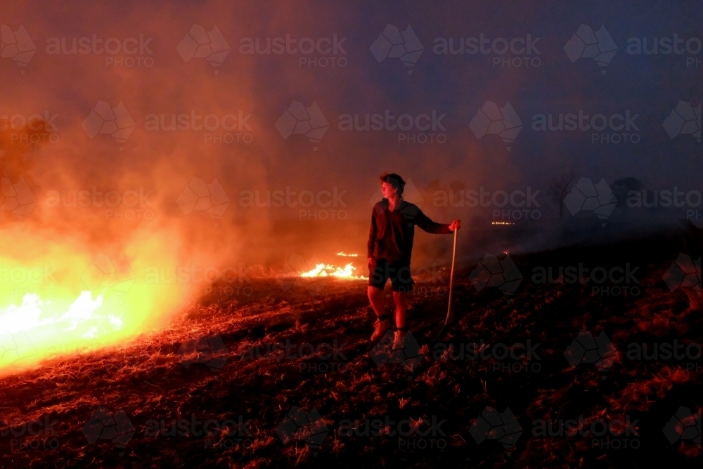 Farmer completing  a Prescribed burn off on the farm showing flames in the night light - Australian Stock Image