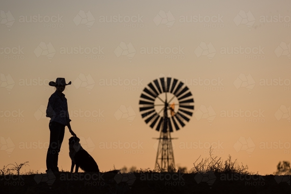 Farmer, dog and windmill in silhouette - Australian Stock Image