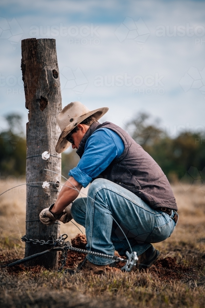 Farmer fencing tying wire to a post - Australian Stock Image
