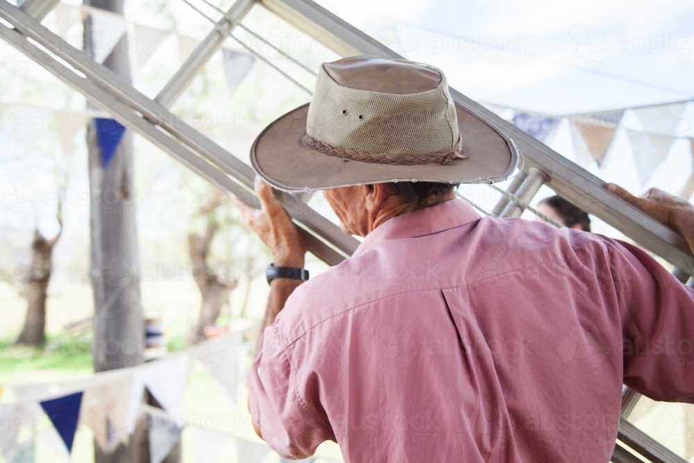 Farmer in a old hat carrying extension ladder - Australian Stock Image