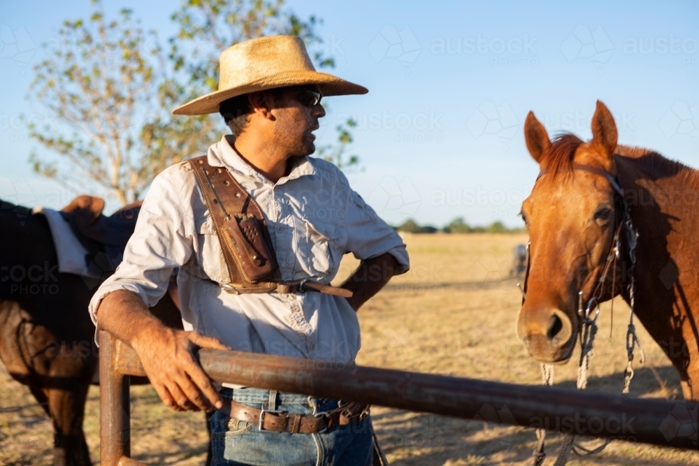 Farmer leaning on a fence near horses - Australian Stock Image
