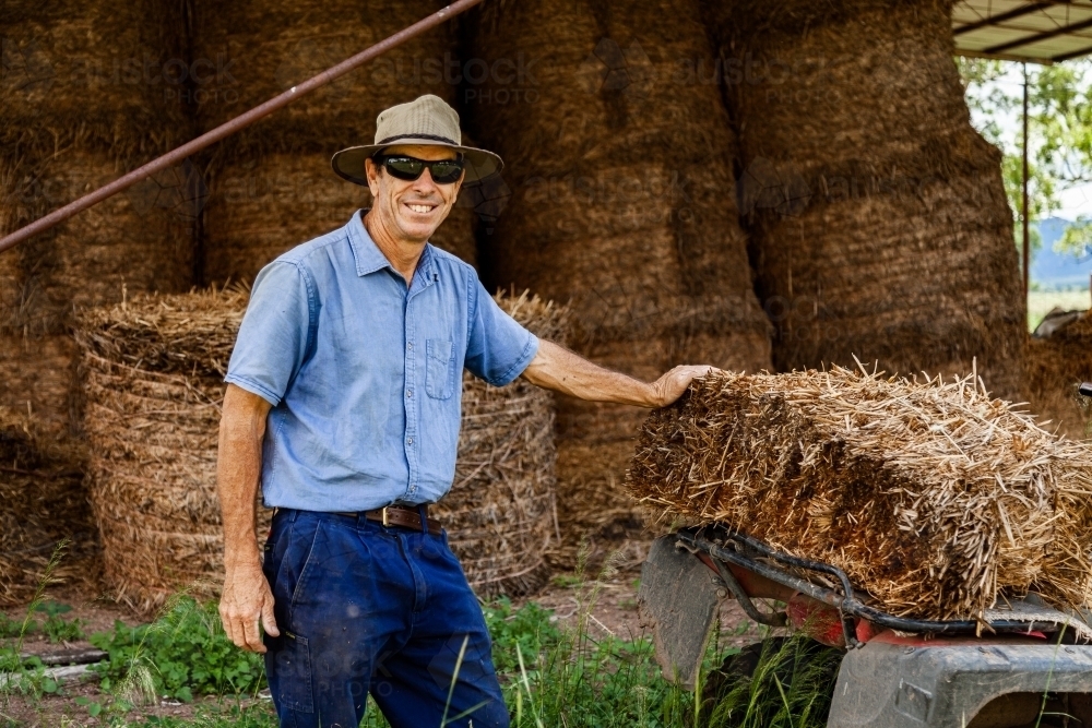 Farmer loading hay bale onto quad bike to feed livestock - Australian Stock Image