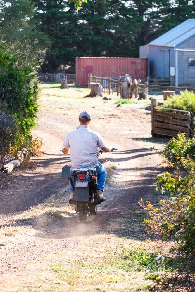 Farmer on motorbike rides down track - Australian Stock Image