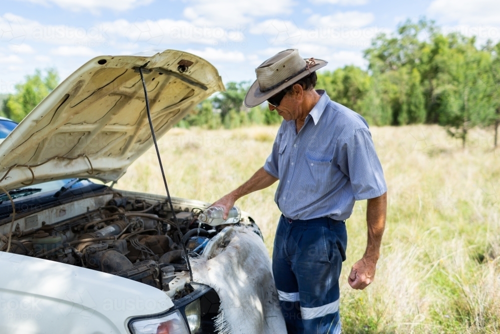 Image of Farmer pouring water on overheating ute car engine in paddock