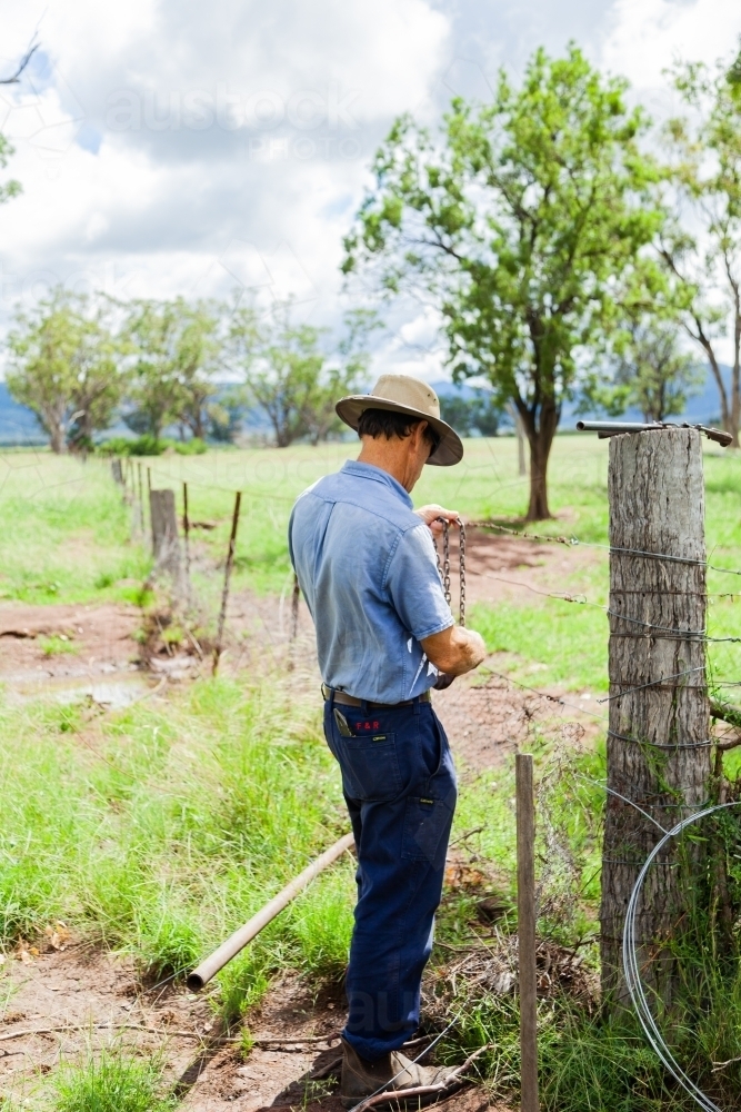Farmer repairing fence so neighbours stock can't get through - Australian Stock Image