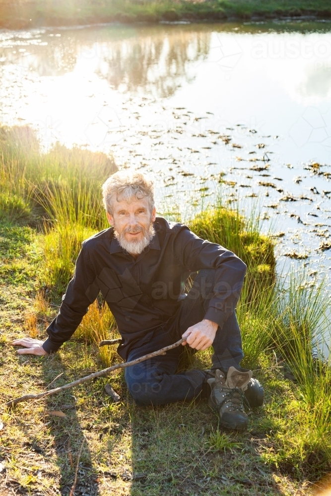 Farmer resting on grass beside dam in paddock - Australian Stock Image